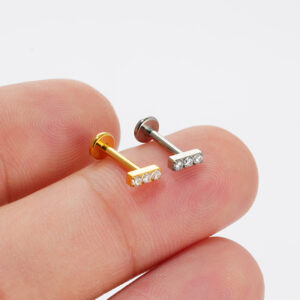 Real-life size scale comparison of Gold and Silver titanium triple gem bar studs held on fingertips.
